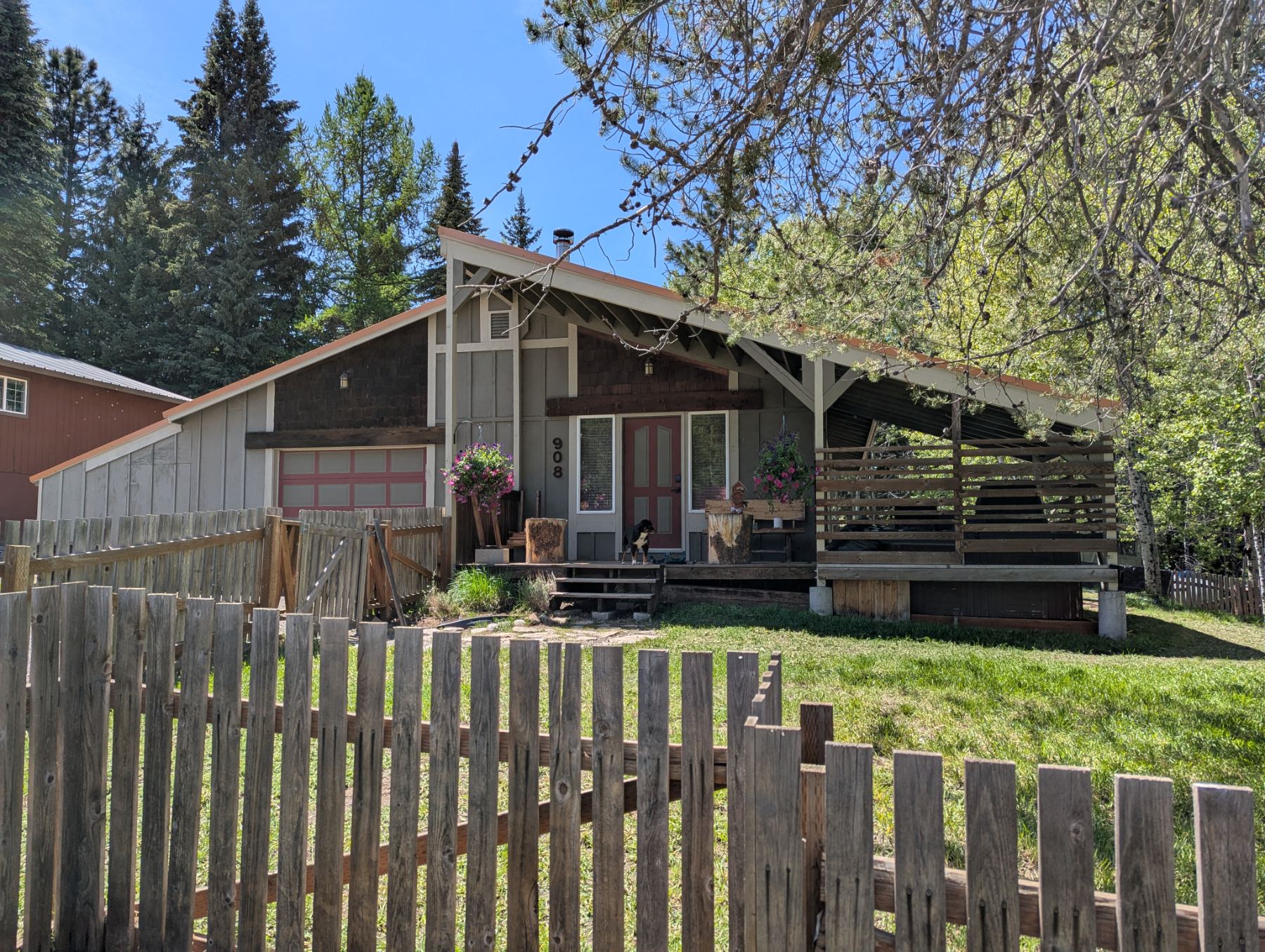 Front of 908 — A-frame cabin with covered porch, red door, surrounded by pines